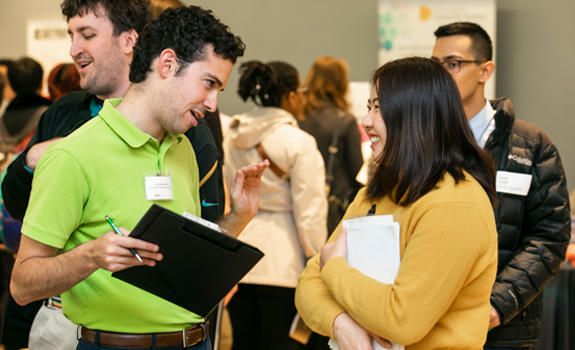 An employer wearing a lime green polo chats with a student wearing a gold-colored sweater at the Part-Time Job Fair.