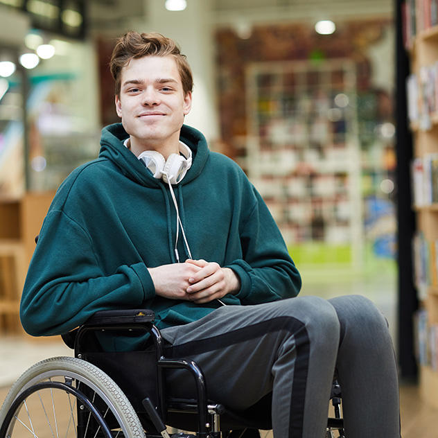 A student using a wheelchair smiles at the camera in the library. 